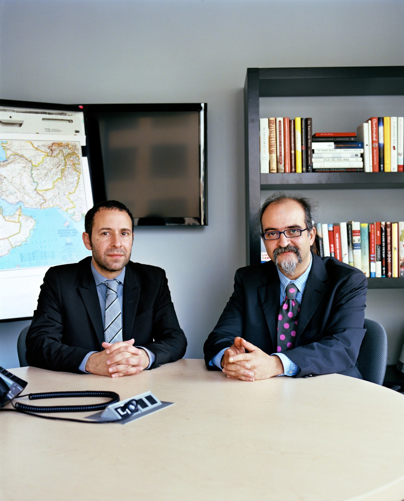 Daniel Levy and Ghaith al-Omari, former Israeli and Palestinian peace negotiators, sitting at a desk in an office with bookshelves and a map behind them.