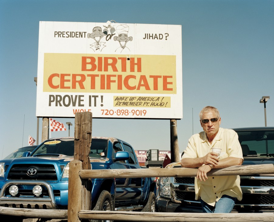 Car dealer Phil Wolf stands beside a controversial billboard questioning President Obama's citizenship and religion at his used-car dealership.