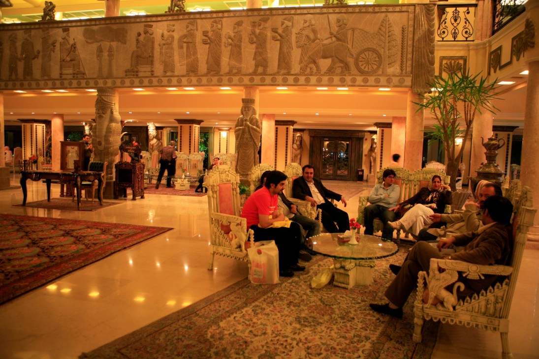 Interior of Dariush hotel lobby with Persian-inspired friezes and statues, guests seated in ornate chairs.