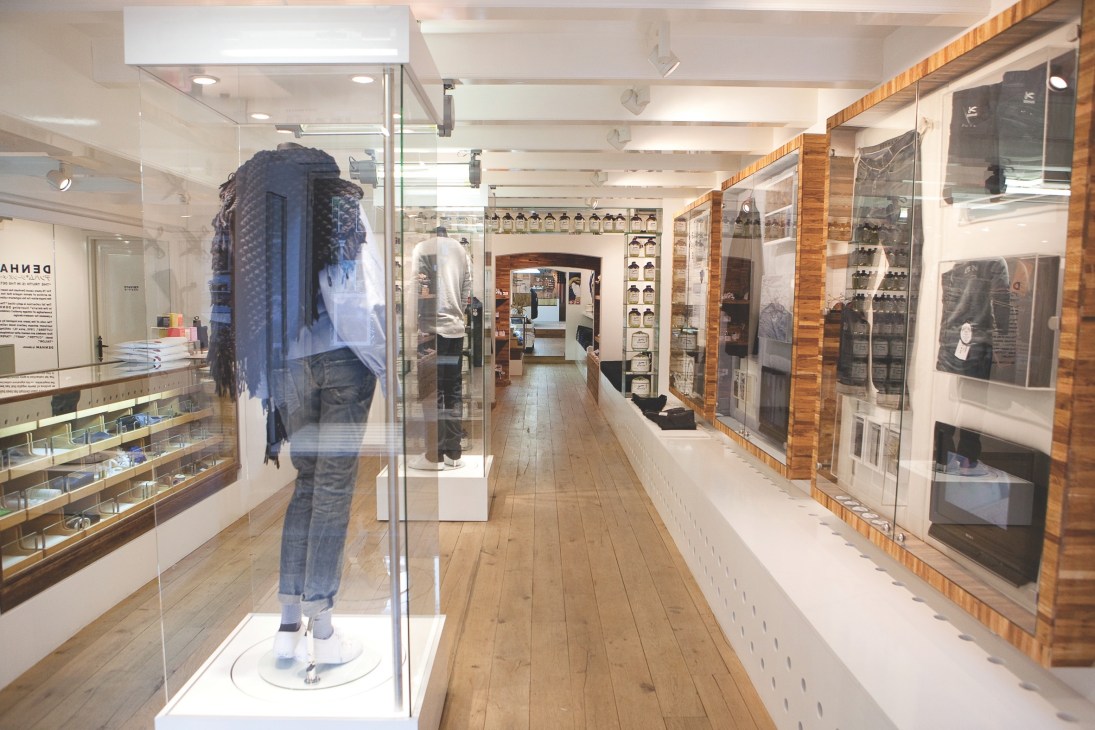 Interior of Denham denim store in Amsterdam with wooden floors, display cases, and mannequin wearing jeans.