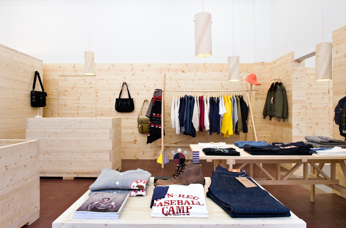 Interior of Mr Mudd & Mr Gold menswear shop in Stockholm with light wood walls, hanging clothes, and displayed accessories.