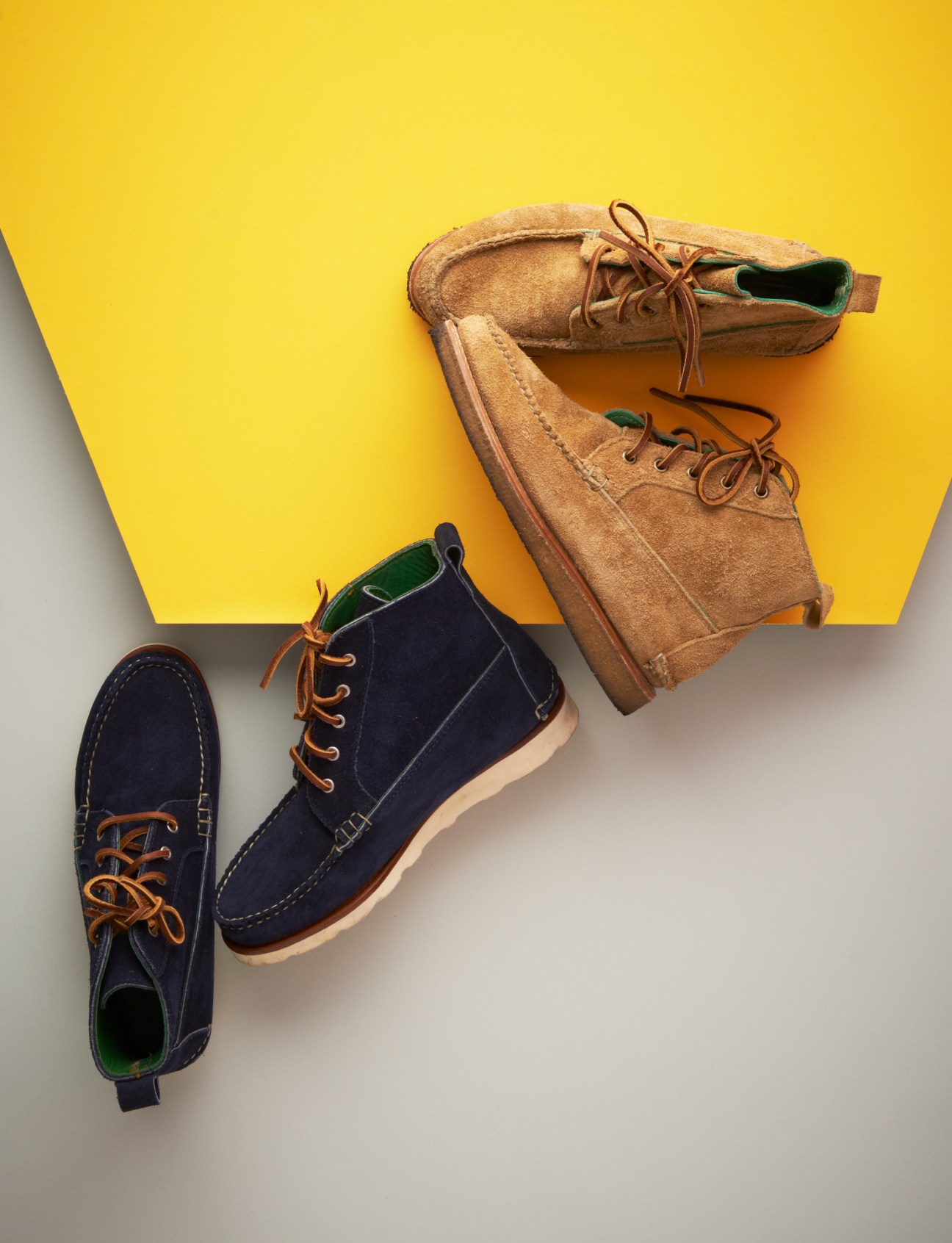 Three suede lace-up boots in navy and tan displayed against a yellow and white background.