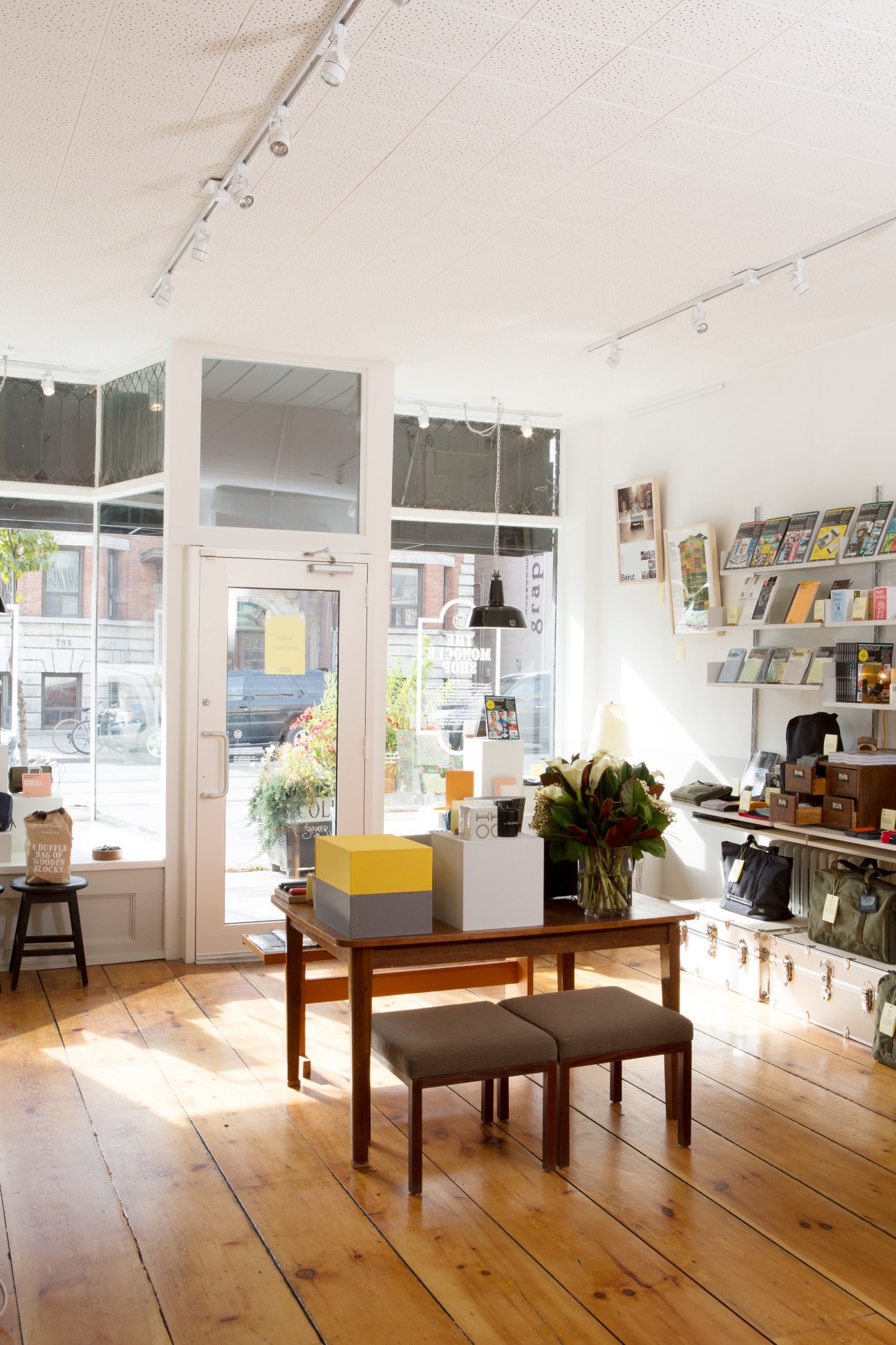 Interior of Monocle's Toronto shop with wooden furniture, shelving, and street view through large windows.