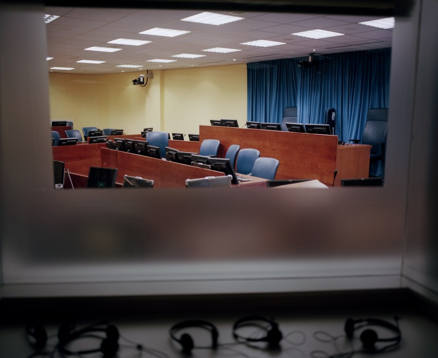 Empty courtroom with wooden judges' bench, blue chairs, yellow walls, and fluorescent lighting at the International Criminal Tribunal for the former Yugoslavia.