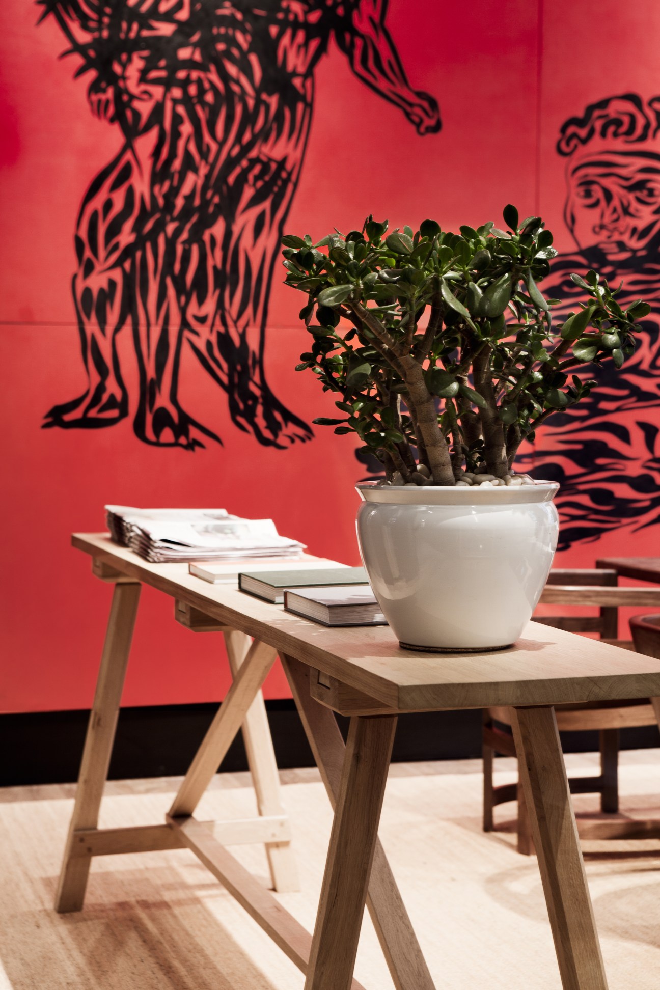 Carlos Capelan mural featuring red and black abstract figures behind a wooden desk with potted plant and magazines.