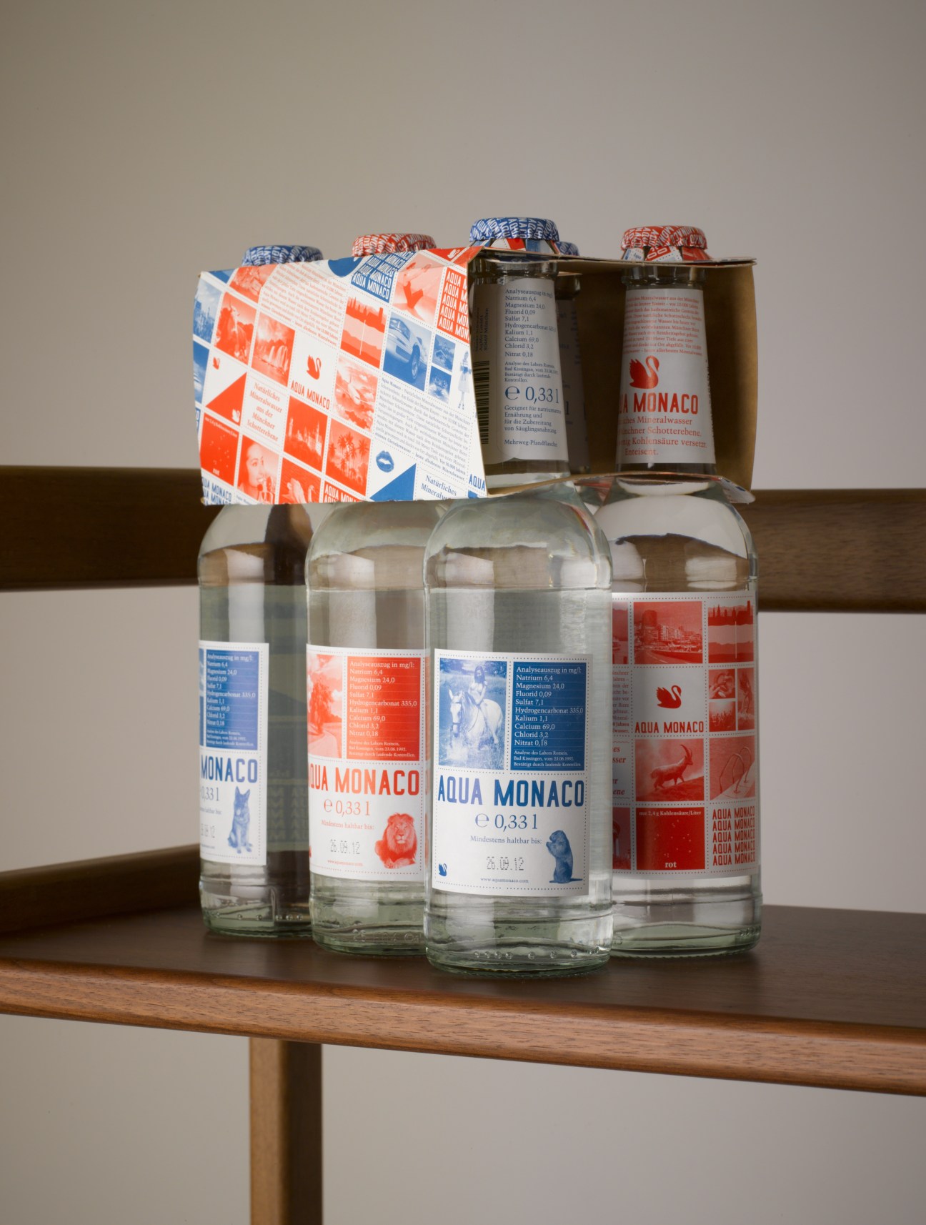 Aqua Monaco water bottles with red and blue labels displayed on a wooden shelf.