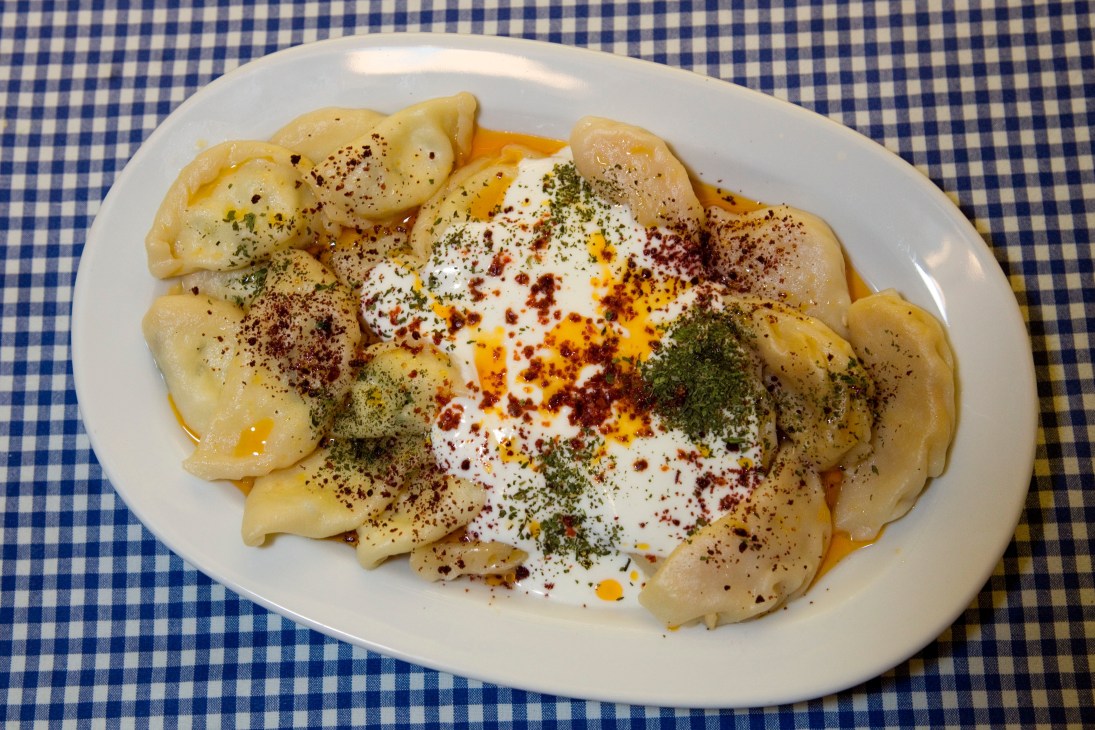 Plate of dumplings topped with white cream, red paprika and green herbs on a blue and white checkered tablecloth.
