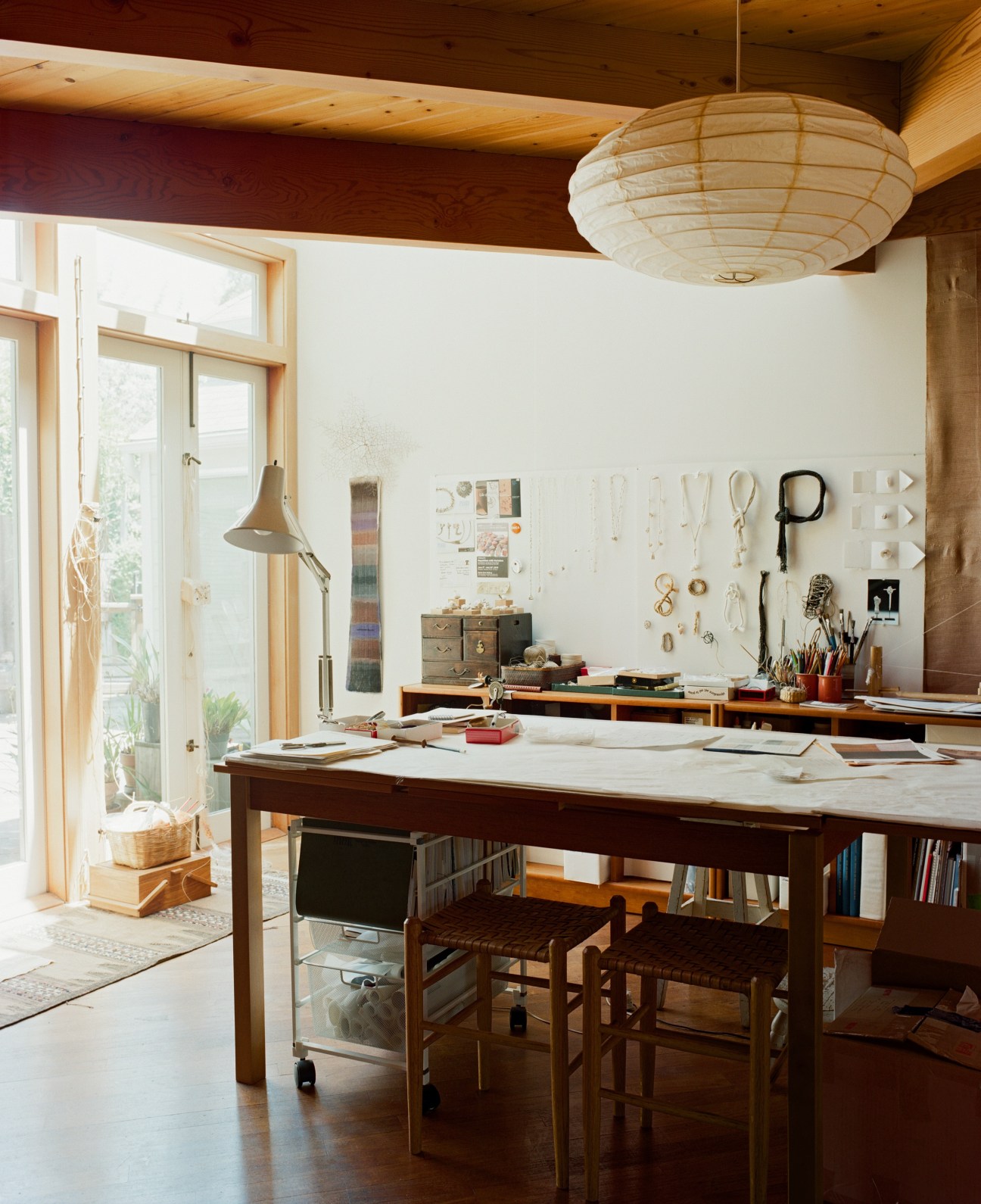 Bright studio space with work table, pegboard wall organizer, natural light, and craft supplies in jars.