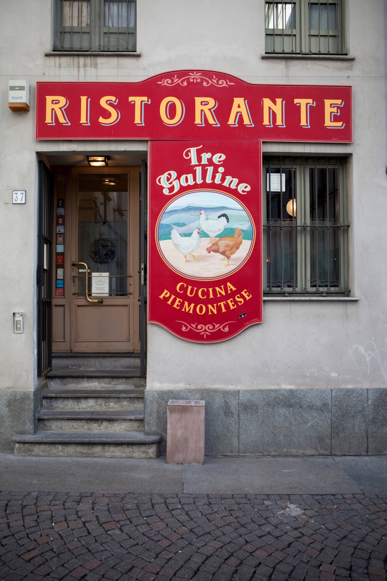 Red storefront of Tre Galline restaurant displaying its name and Piedmontese cuisine sign in Turin.