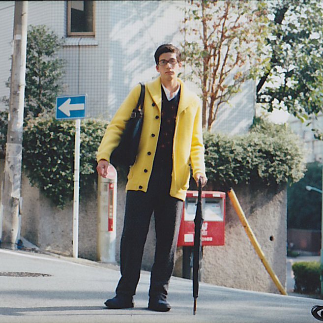 Man in yellow cardigan and black trousers holding umbrella on urban street