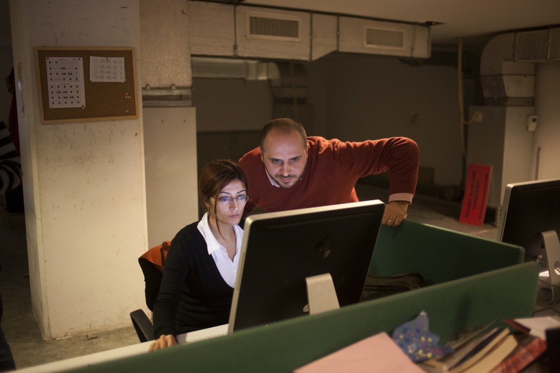 Two journalists working together at a computer desk in a newspaper office.