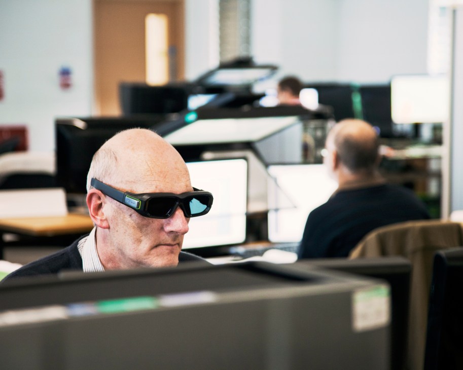 Man wearing stereoscopic glasses at a computer workstation in an office environment.