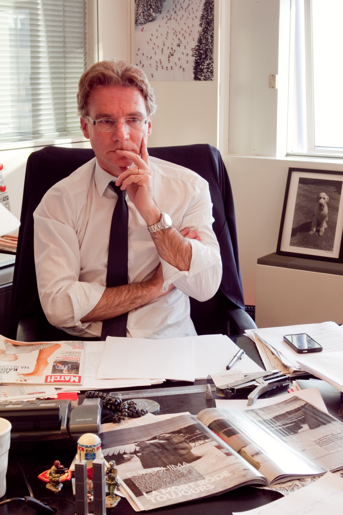 Olivier Royant, editor-in-chief of Paris Match, sits at his desk surrounded by magazine layouts and materials.