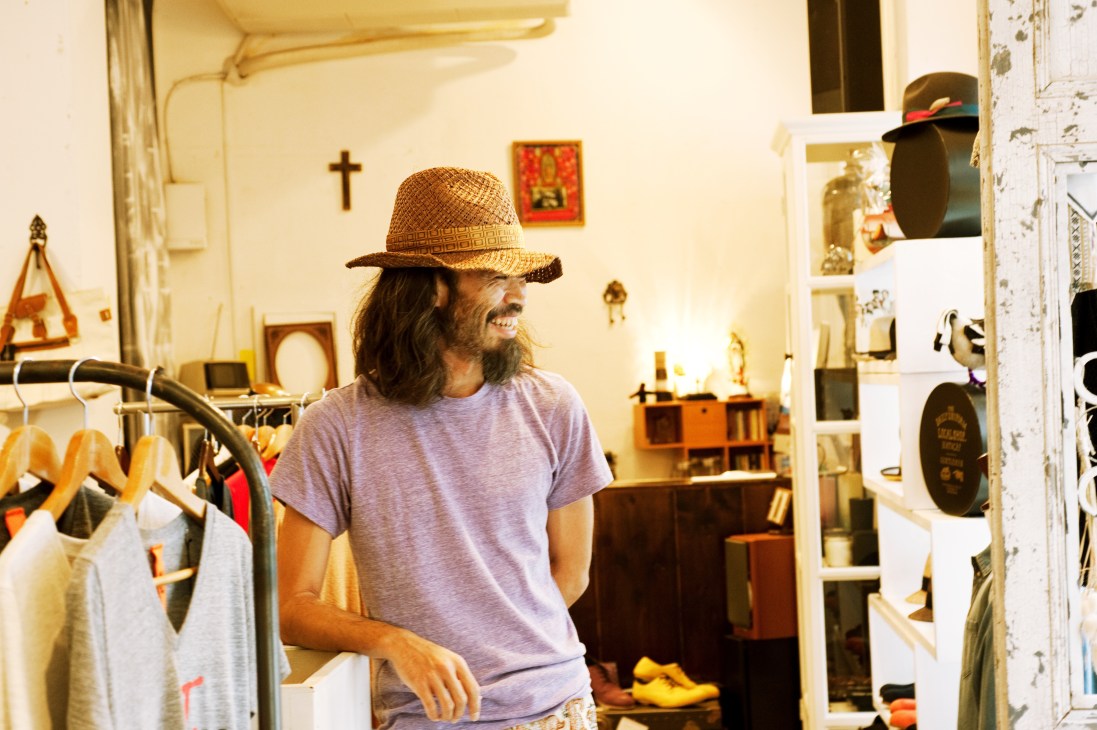 Man wearing straw hat and purple t-shirt inside clothing shop with shelves and hanging garments