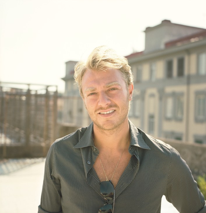 Giampaolo Valerio, a property manager in Vomero, smiles at the camera on a rooftop terrace with classical architecture behind him.