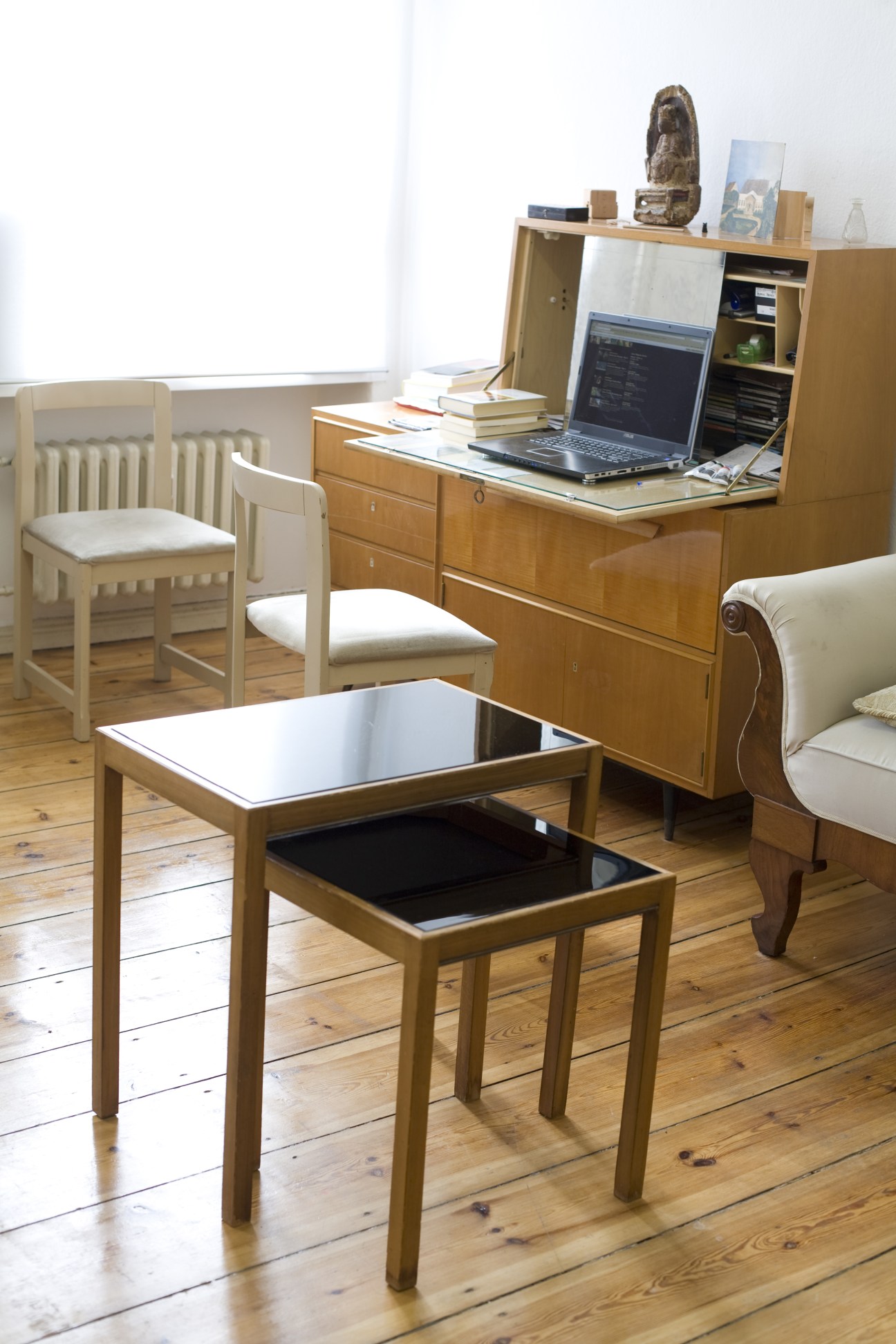Minimalist home office and living area with wooden furniture, laptop desk, and mid-century chairs.