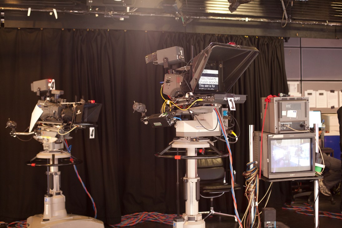 Television studio setup with professional camera equipment, teleprompter, and monitoring screens.