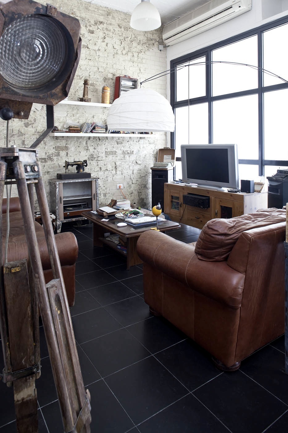 Industrial-style apartment interior with exposed brick walls, leather armchairs, vintage lighting, and eclectic furnishings.