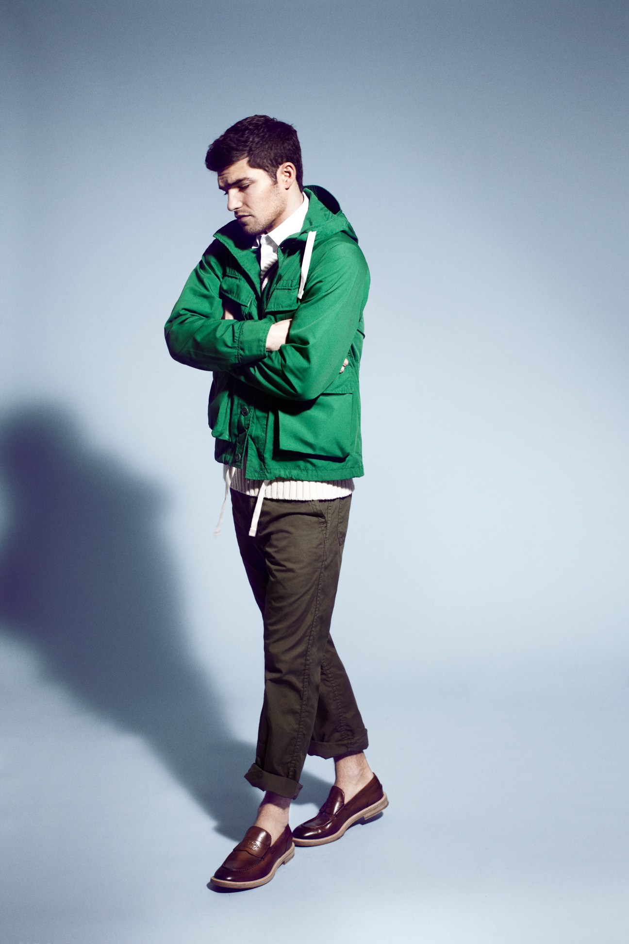Male model wearing green Woolrich Woolen Mills jacket, Polo Ralph Lauren knit vest, Lacoste polo shirt, White Mountaineering trousers, and Gucci shoes.