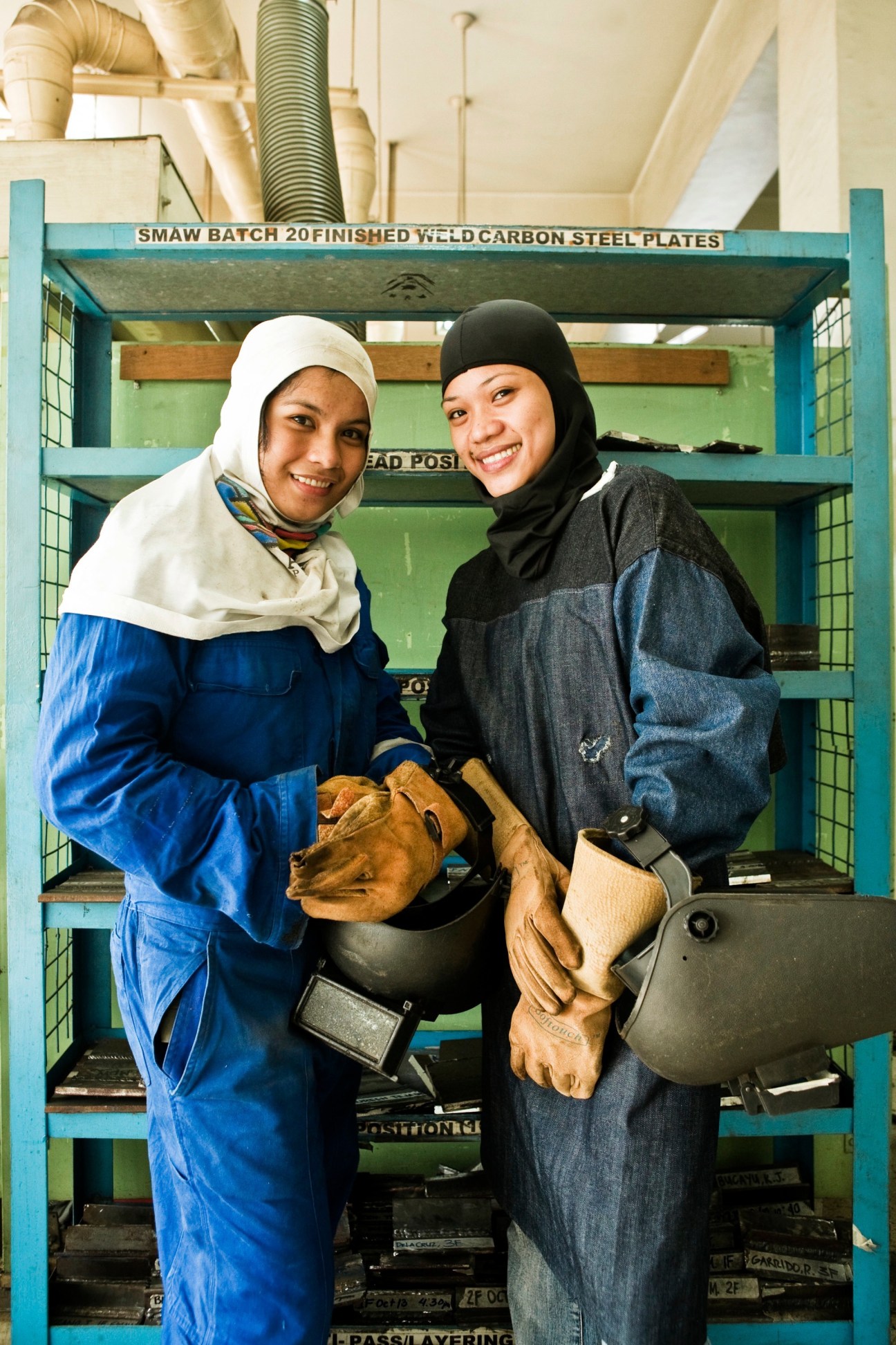 Two female welding students in protective gear smiling at a Tesda training facility.