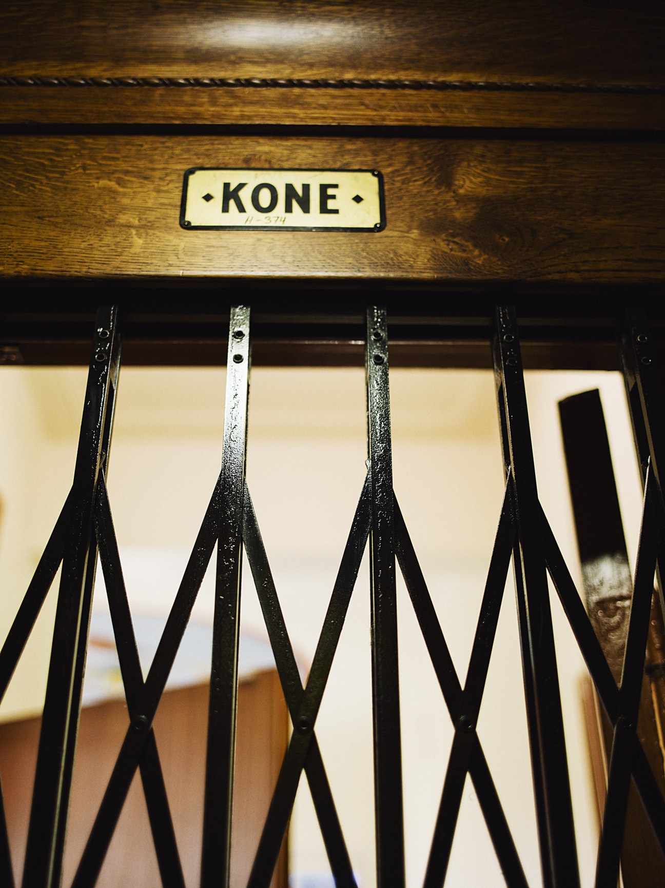 Vintage Kone elevator with wooden paneling and concertina metal grille door.