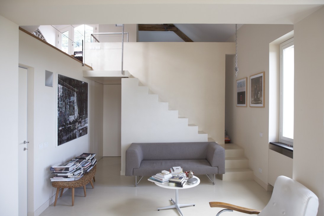 Modernist interior of Villa Rosmarino featuring a gray sofa, white staircase, and natural light from large windows.