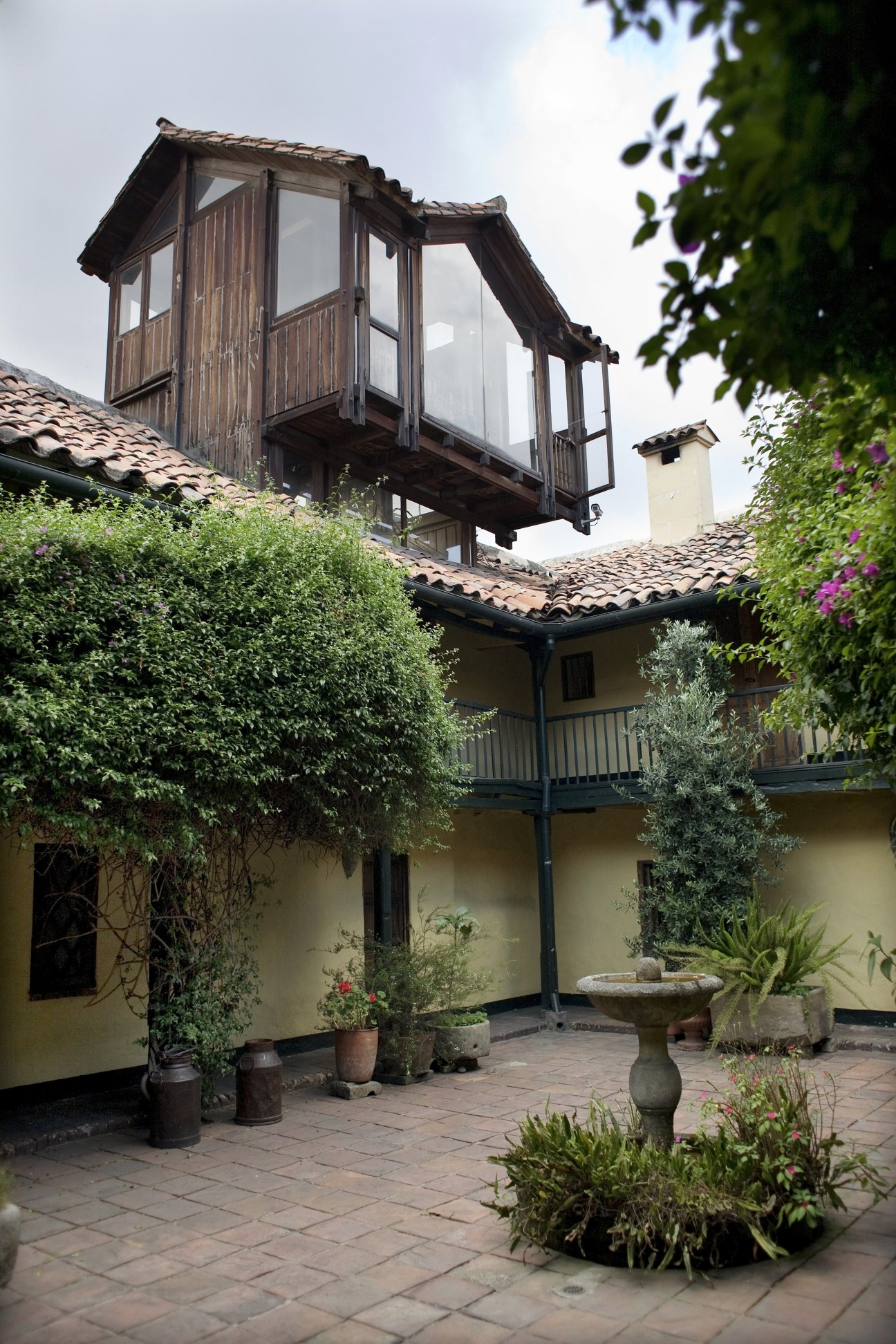 Colonial courtyard with terracotta tiles, yellow walls, wooden balcony and climbing ivy plants.