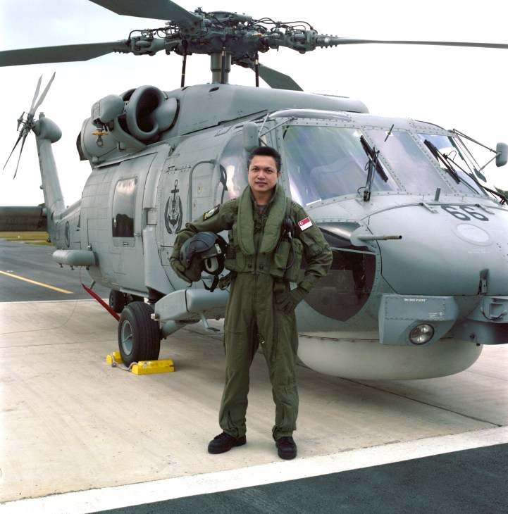 Senior Lieutenant Colonel Jonathan Tan in flight suit stands before a military helicopter on tarmac.