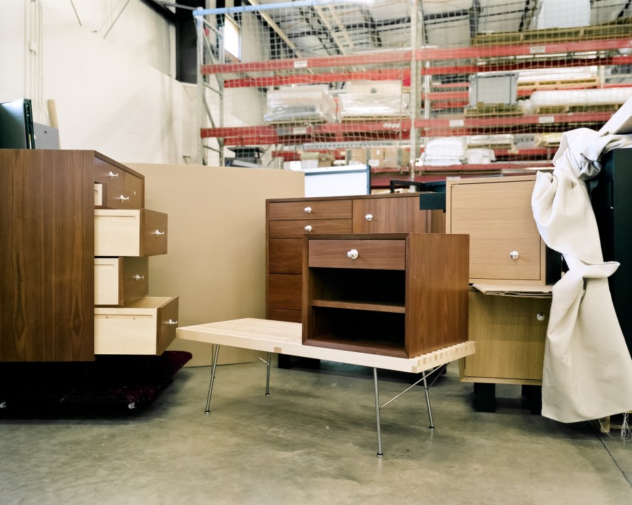 Reissued mid-century modern wooden furniture pieces by George Nelson displayed in a warehouse facility.