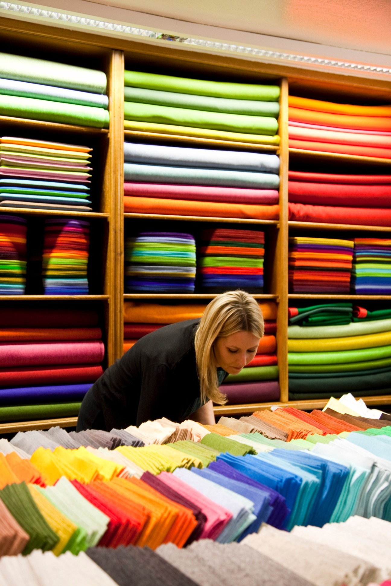 Woman browsing colorful fabric rolls displayed on wooden shelves in Johanna Daimer shop.