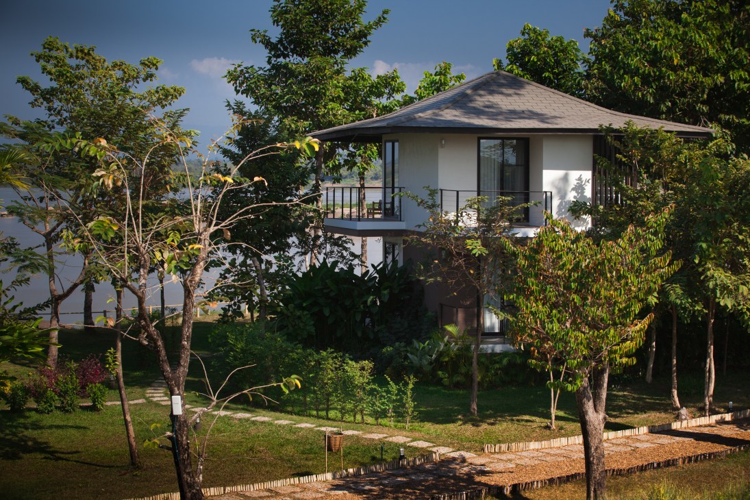 Modern riverside villa with Japanese-inspired architecture surrounded by lush gardens and trees in Laos.