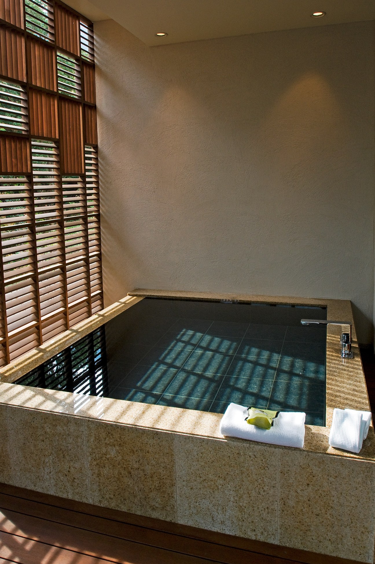 A private stone bath at Sankara Hotel with wooden shutters and natural light filtering through.