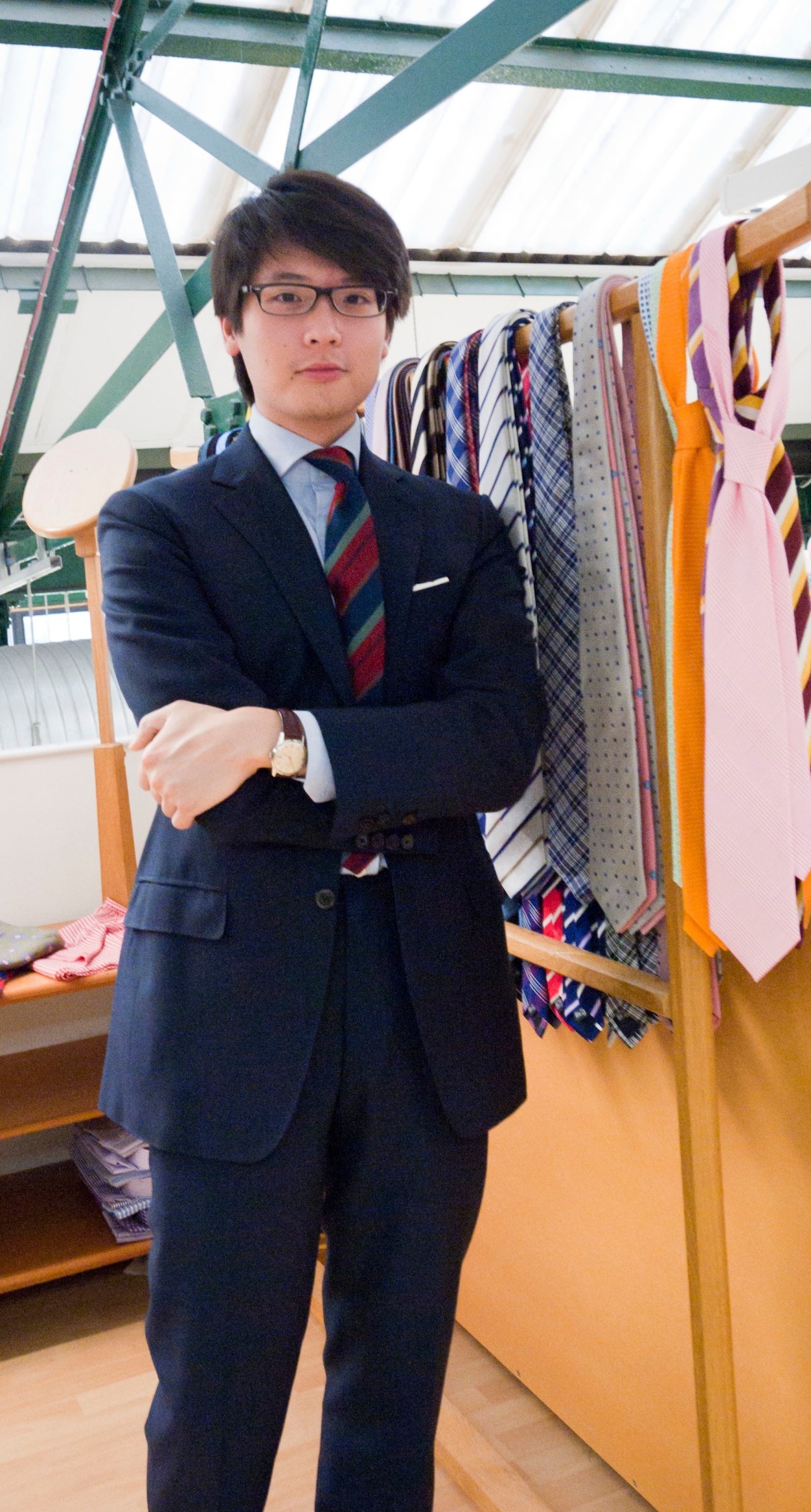 Man in navy blazer and striped tie standing in front of displayed neckties at The Armoury menswear store in Hong Kong.