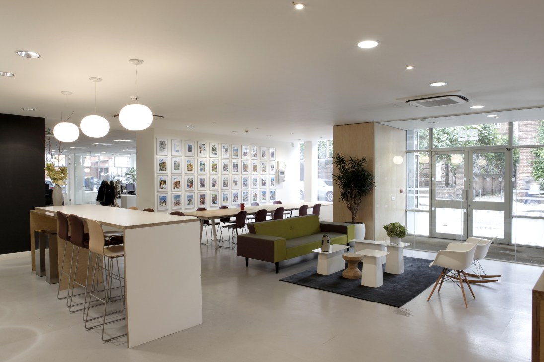 Modern office entrance hall with white counter, green sofa, pendant lighting, and wall of framed photographs.
