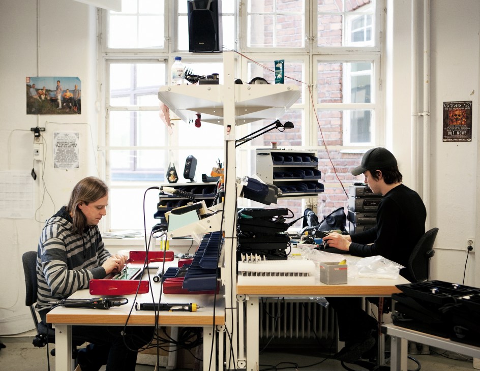 Two staff members assemble and test Nord keyboards at workbenches in a Stockholm factory.