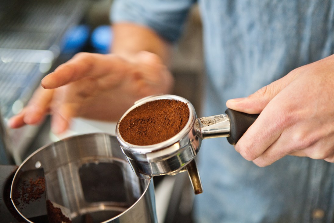 Barista holding a portafilter filled with ground coffee powder during espresso preparation.