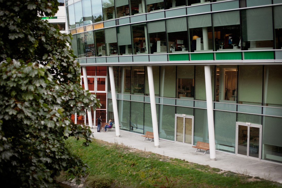 Modern multi-story building exterior with green and red panels, white columns, and ground-level seating area.
