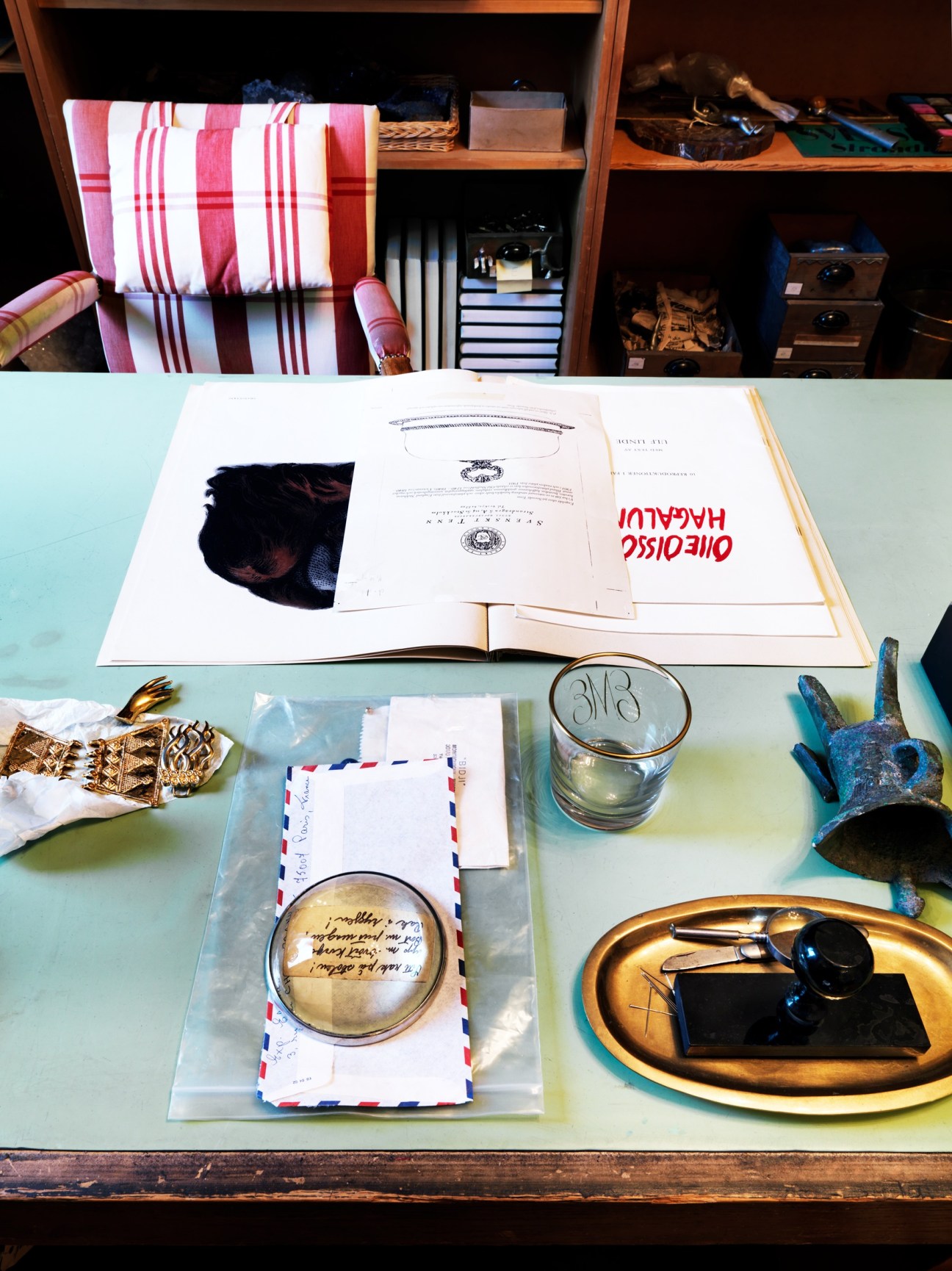 Desktop in Estrid Ericson's recreated office displaying books, correspondence, decorative objects and brass accessories on a light blue surface.