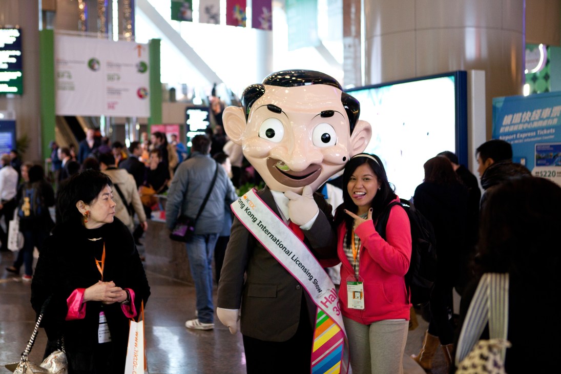 A visitor poses with a large cartoon character mascot at the Hong Kong Toys & Games Fair.