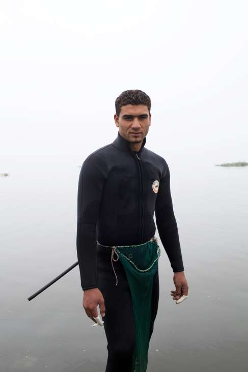Young man in wetsuit holding fishing net stands in shallow water near Ismailia.