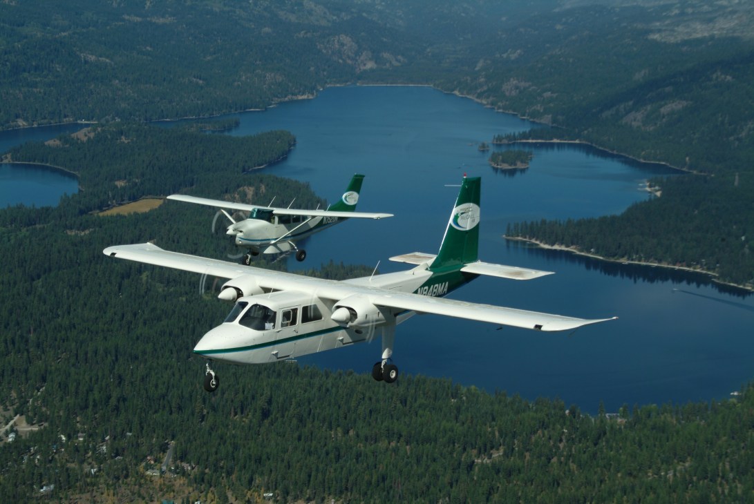 Salmon Air aircraft flying over forested wilderness with a pristine blue lake below.