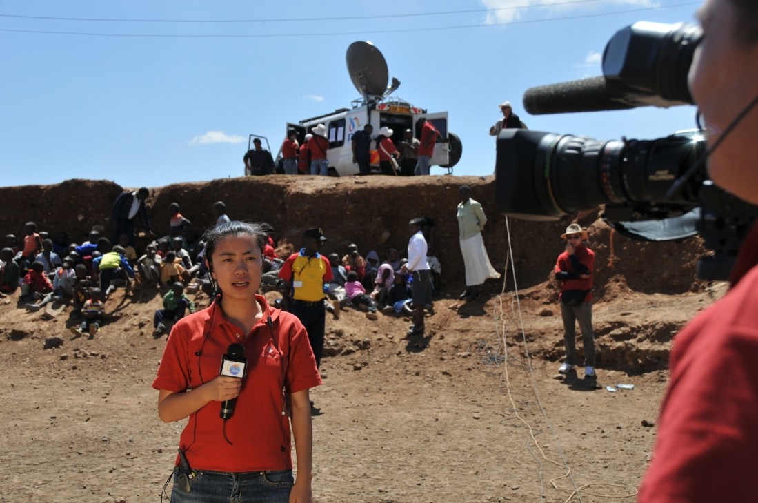 CNC correspondent Wang Lu reporting from Kenya with camera crew and local crowd in background.