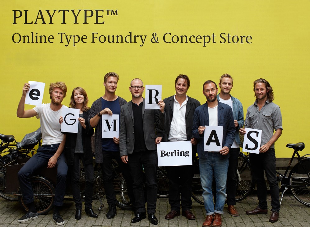 E-Types staff holding large letter cards spelling out font names against a bright yellow wall with bikes.