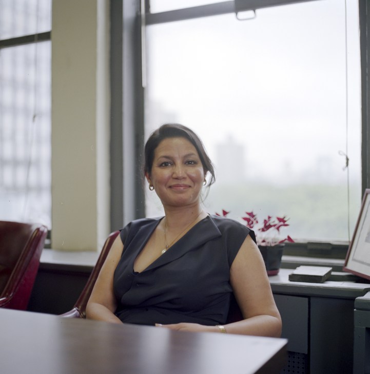 Purnima Kapur, director of the Brooklyn office, sits at a desk in a modern office with large windows overlooking the city.