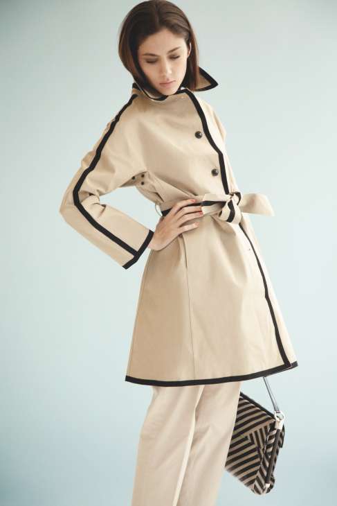 Woman wearing a beige Mackintosh coat with black trim and matching striped clutch bag.