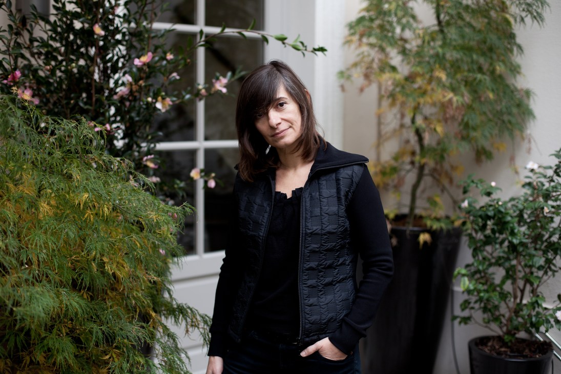 Sara Deux, artistic director at XXI magazine, standing in a courtyard surrounded by green plants and pink flowers.