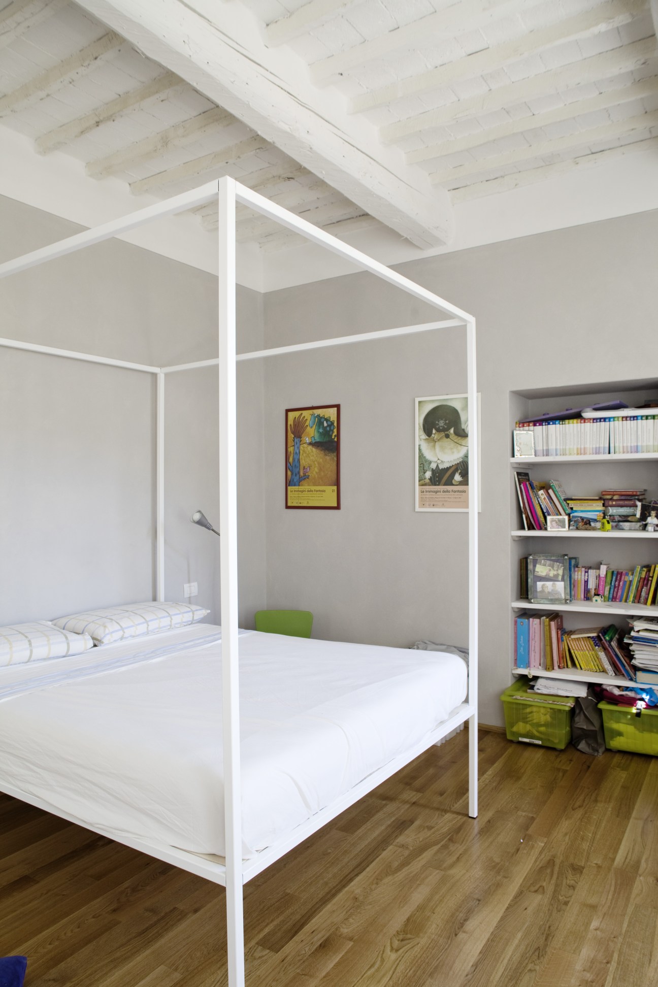Modern minimalist bedroom with white four-poster bed, exposed wooden beams, and built-in bookshelf.