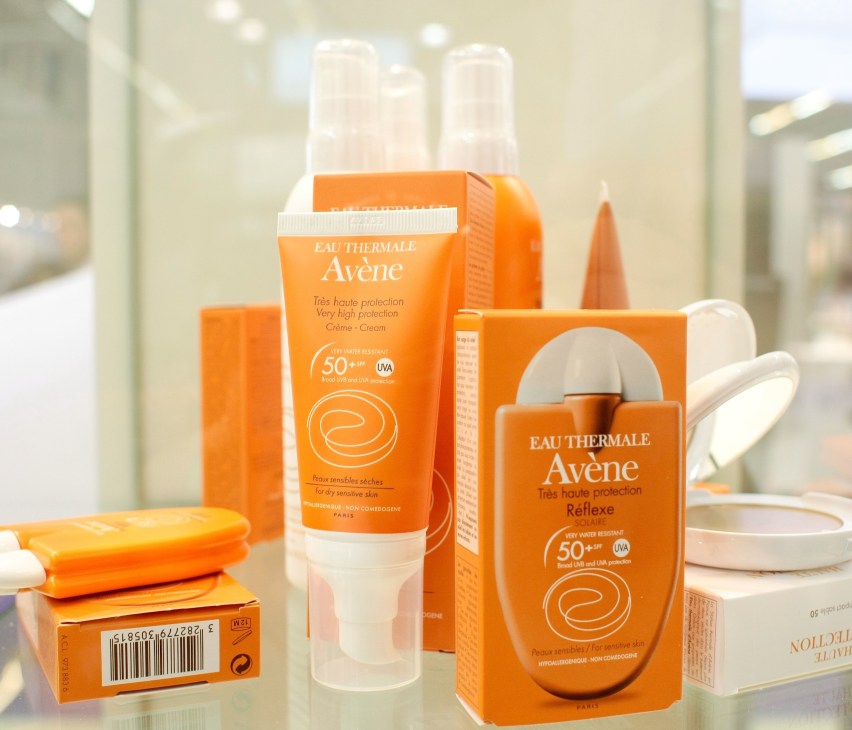 Range of Avène sunscreen and skincare products in orange packaging displayed on a bathroom counter.