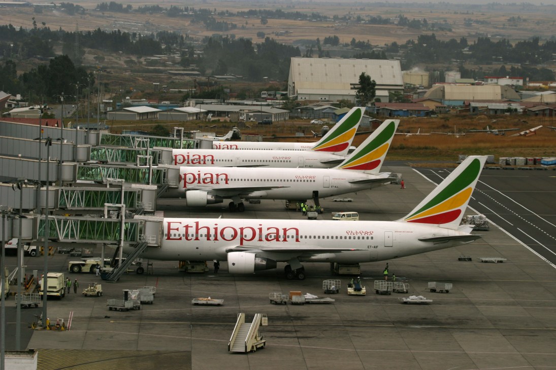 Ethiopian Airlines aircraft parked at Bole International Airport with terminal buildings and countryside landscape in background.
