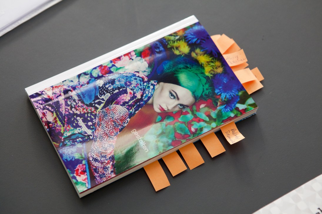 A colorful art book with vibrant floral and portrait imagery on its cover, marked with orange page tabs.
